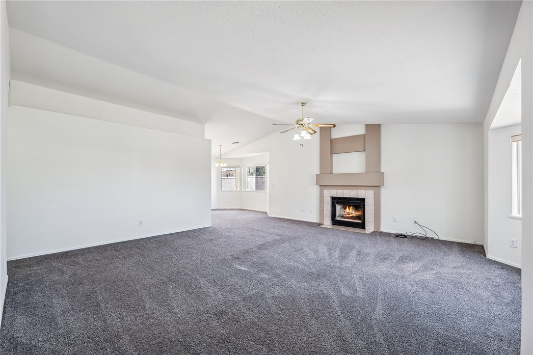 2524 South Ridge Avenue Bullhead City, AZ 86429 - Photo 11 of 64 Unfurnished living room with lofted ceiling, a tiled fireplace, carpet floors, a ceiling fan, and baseboards