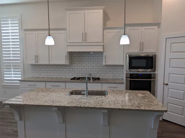a kitchen with stainless steel appliances granite countertop a sink a microwave and a white wooden cabinets