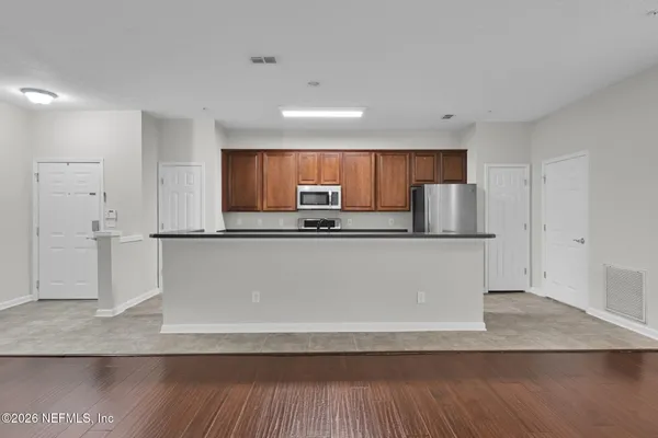 a kitchen with stainless steel appliances granite countertop a refrigerator a sink a stove a microwave and white cabinets with wooden floor