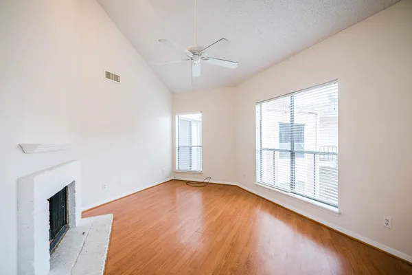 an empty room with wooden floor fan and windows