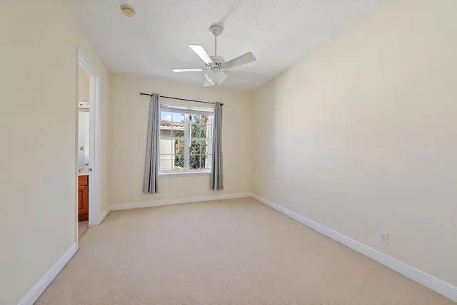 an empty room with chandelier fan and windows