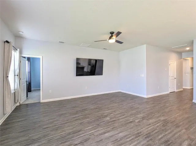 a view of an empty room with wooden floor and a ceiling fan