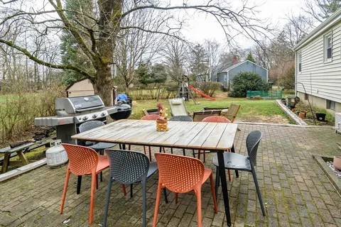 a view of a patio with table and chairs under an umbrella with large trees