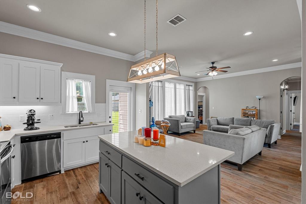 6896 Bethany Reed Circle Blanchard, LA 71107 - Photo 24 of 37 Open-concept living area featuring a kitchen island with a light-toned countertop, white cabinetry with black hardware, stainless steel appliances, and wood-finish flooring