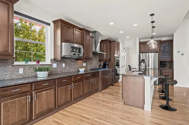 a kitchen with stainless steel appliances granite countertop wooden cabinets a sink a stove a refrigerator and dishwasher with wooden floor