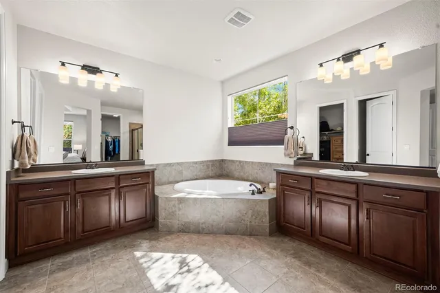 a spacious bathroom with a tub a double vanity sink and a large mirror