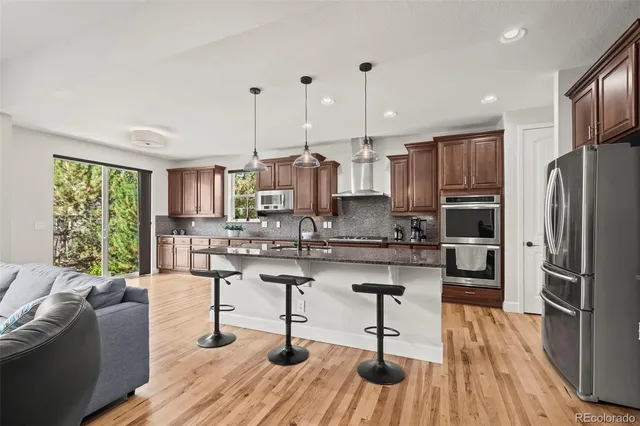 a kitchen with stainless steel appliances granite countertop a refrigerator a stove a sink dishwasher a couches and chairs with wooden floor