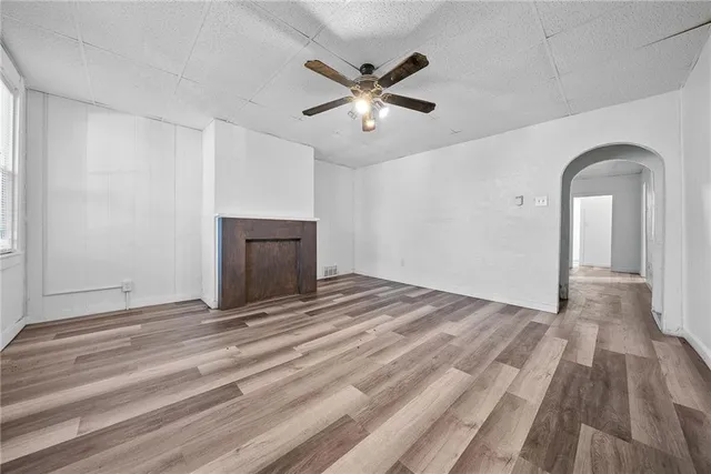 a view of an empty room with wooden floor and a ceiling fan