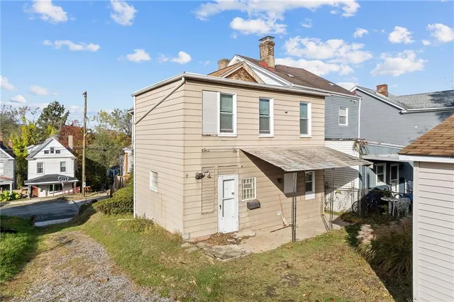 a view of a white house next to a yard with plants and large trees