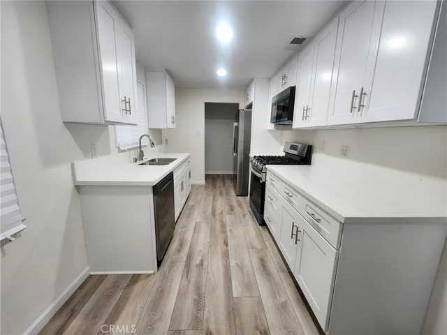 a kitchen with white cabinets stainless steel appliances a sink and wooden floor