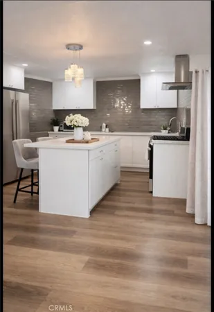 a large white kitchen with kitchen island a stove a sink dishwasher and white cabinets with wooden floor
