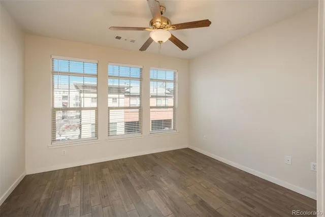 an empty room with wooden floor fan and windows
