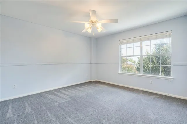 an empty room with a chandelier fan and windows