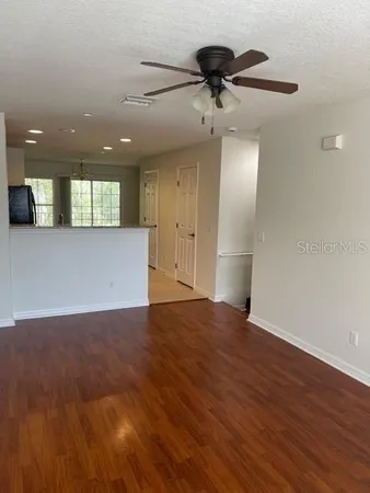 a view of an empty room with wooden floor and a ceiling fan