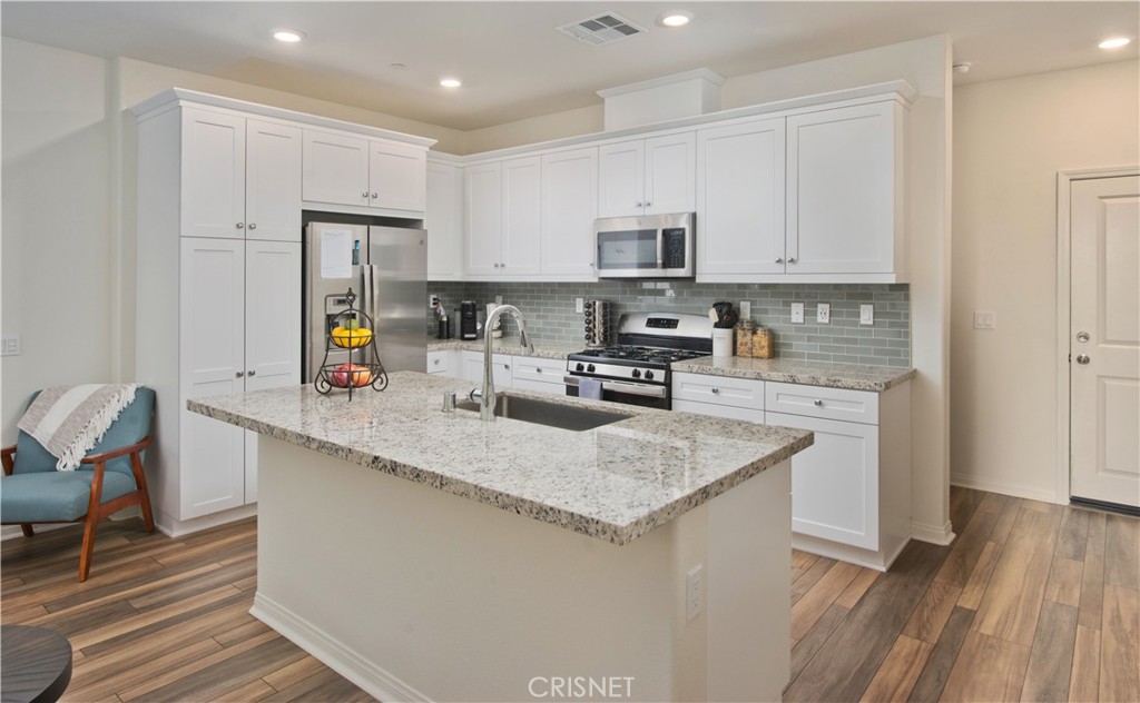 22880 Concord Drive Saugus, CA 91350 - Photo 10 of 34 a kitchen with stainless steel appliances granite countertop a sink dishwasher a refrigerator a microwave oven with white cabinets and wooden floor