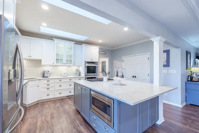 a kitchen with stainless steel appliances granite countertop a refrigerator a sink dishwasher a stove and white cabinets with wooden floor