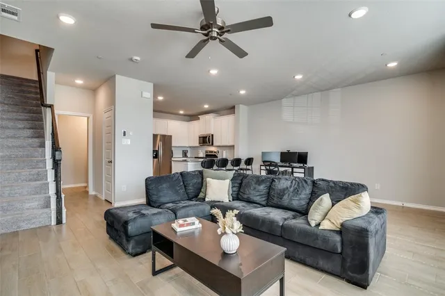 a living room with furniture kitchen area and a ceiling fan