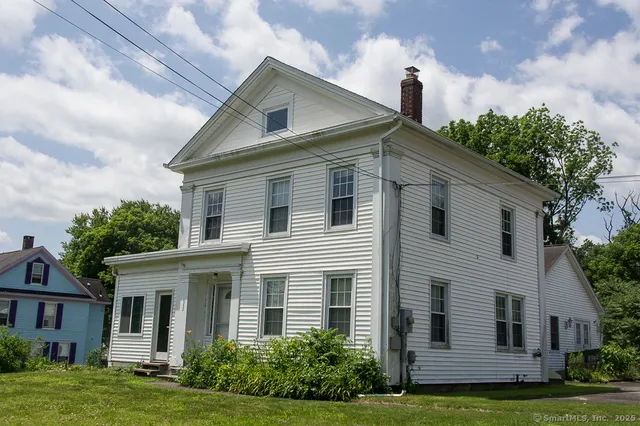 a view of a white house next to a yard with plants and trees