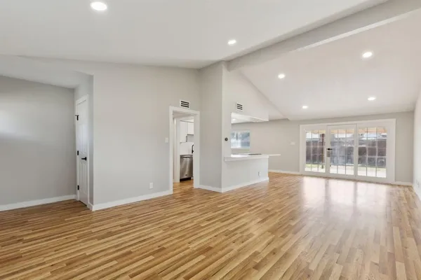 a view of an empty room with wooden floor and a kitchen