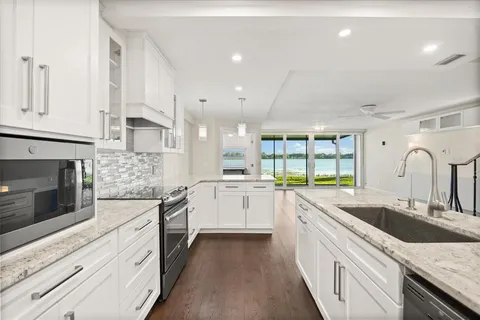 a kitchen with stainless steel appliances kitchen island granite countertop a stove a sink a refrigerator and white cabinets with wooden floor