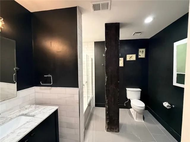 a bathroom with a granite countertop sink a toilet a mirror and shower