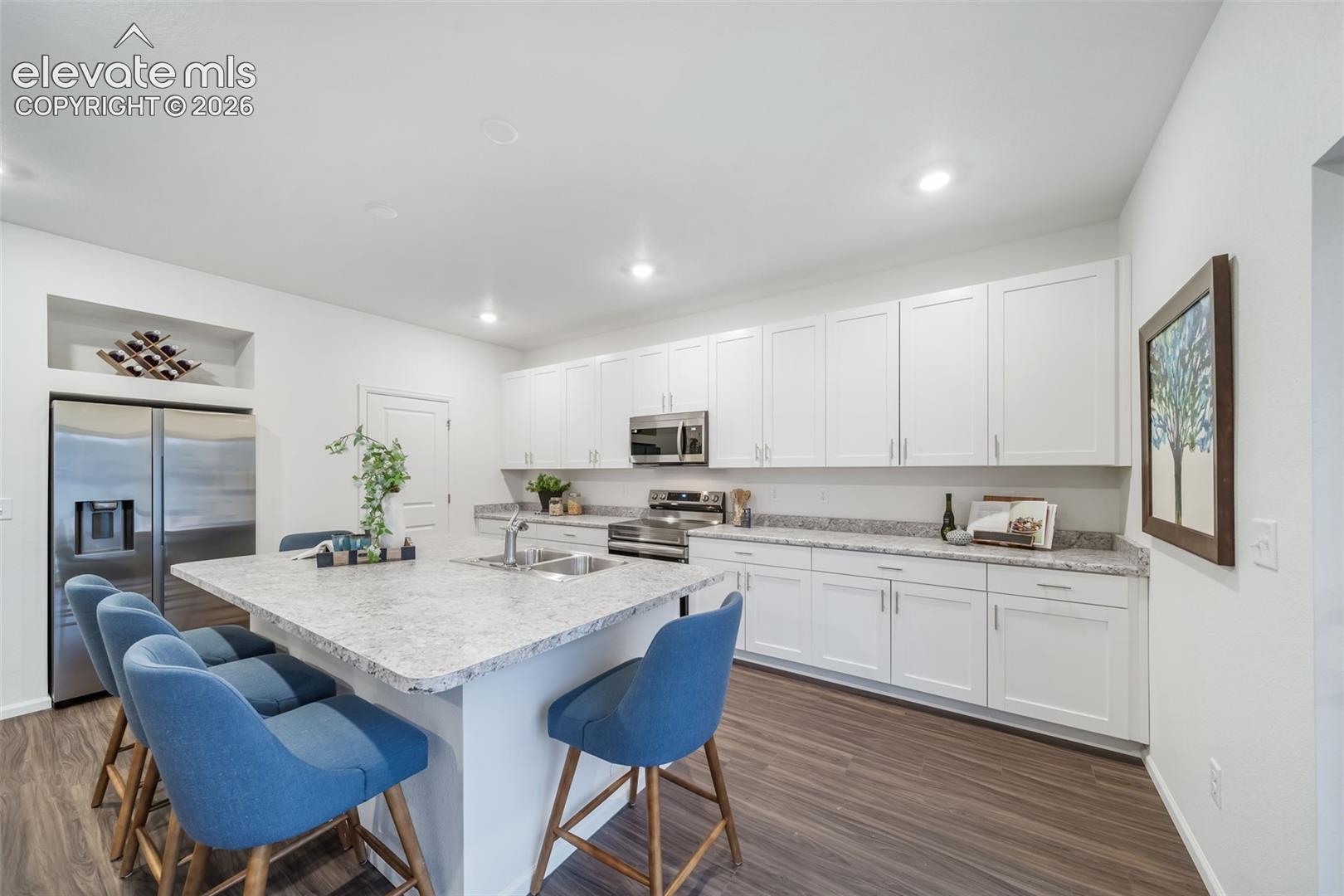 4936 Truscott Road Colorado Springs, CO 80925 - Photo 26 of 41 Modern kitchen featuring a large island with an integrated sink, white cabinetry, stainless steel appliances, and wood-finish flooring
*photos of a model home*