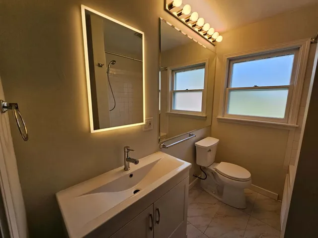 a bathroom with a sink mirror toilet and next to a window