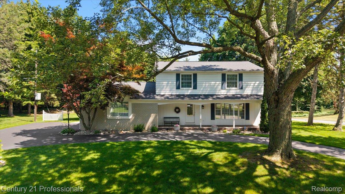 633 Foxhall Road Bloomfield Hills, MI 48304 - Photo 2 of 61 Two-story colonial residence featuring white siding and dark shutters, a covered front porch, a paved circular driveway, mature trees, and a manicured lawn