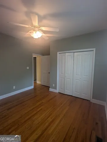 a view of an empty room with wooden floor and a fan