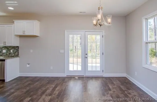 an empty room with wooden floor chandelier and windows