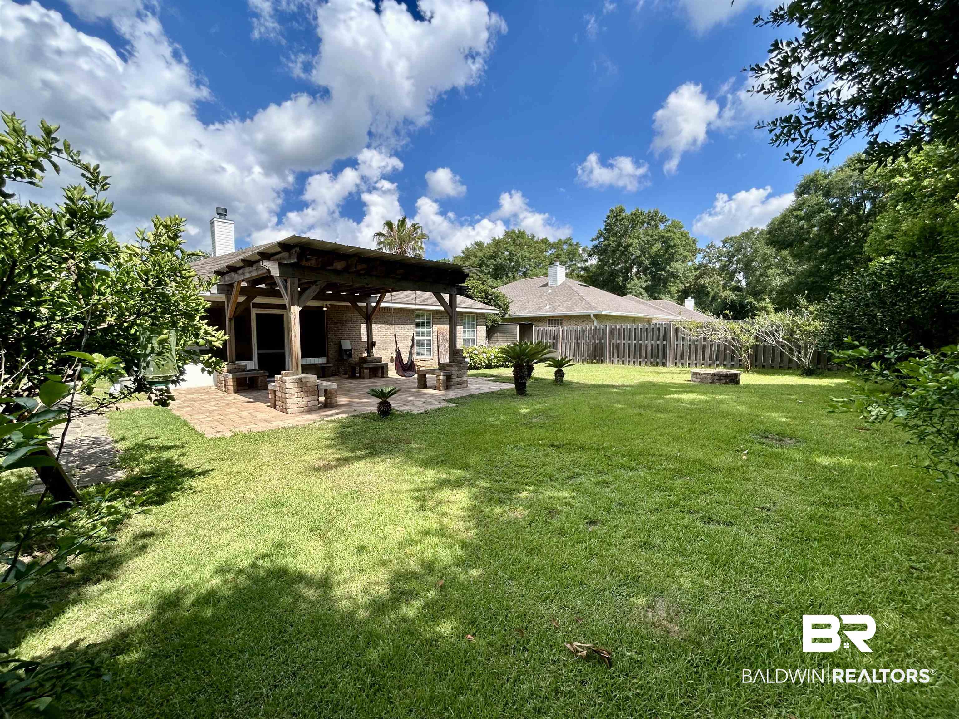 7198 Raintree Lane Gulf Shores, AL 36542 - Photo 32 of 33 Expansive backyard featuring a brick paver patio, a wooden pergola structure, and a dedicated fire pit area