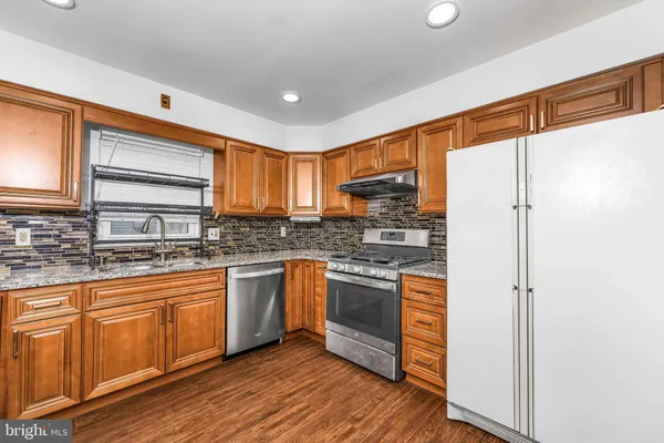 a kitchen with stainless steel appliances granite countertop a refrigerator a stove top oven a sink and dishwasher with wooden floor