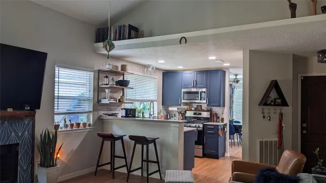 a kitchen with stainless steel appliances kitchen island granite countertop a refrigerator a stove a sink a dining table and chairs with wooden floor