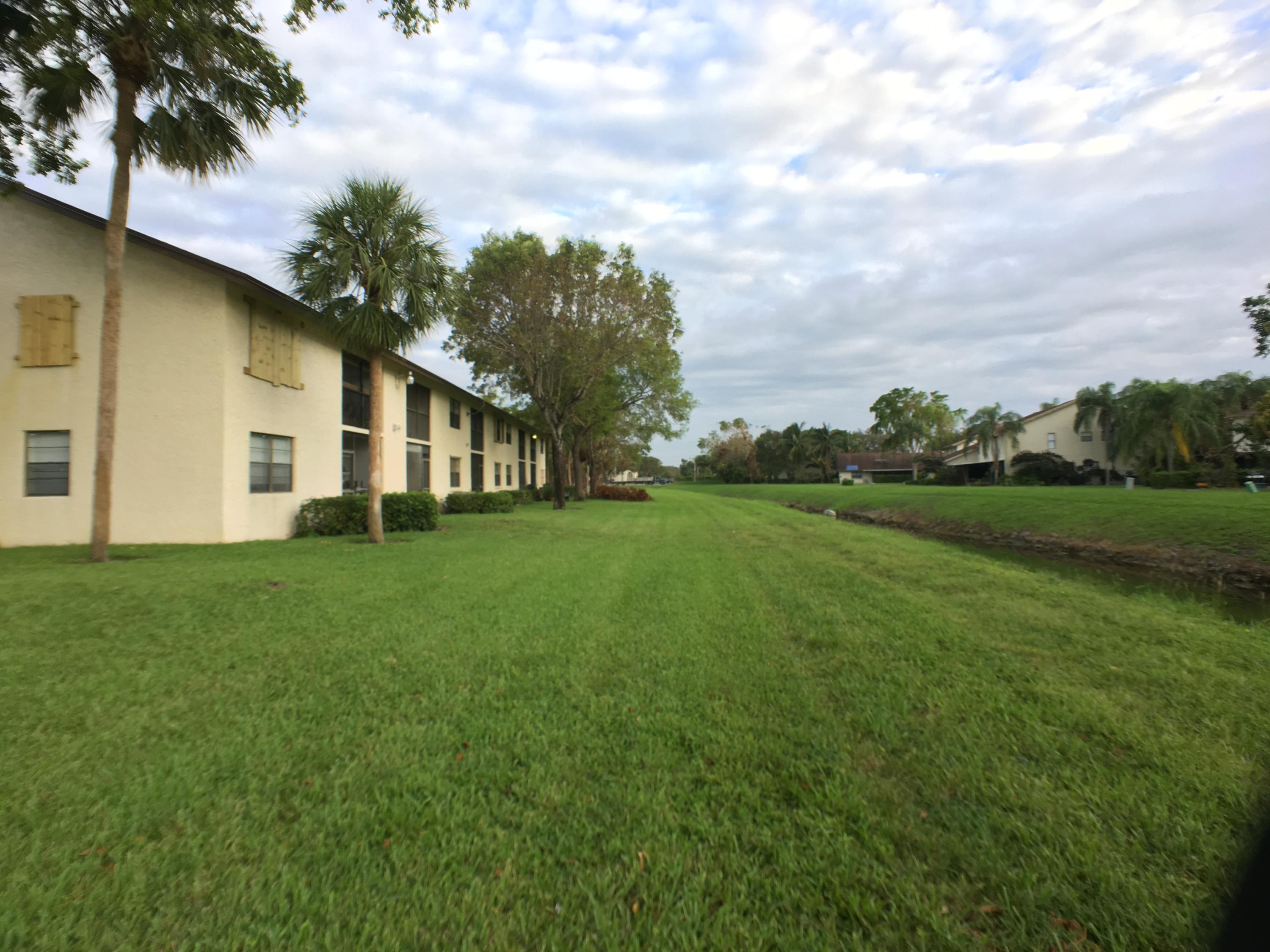 23398 Southwest 57th Avenue, Unit 309 Boca Raton, FL 33428 - Photo 27 of 29 a view of a white house in front of a big yard with plants and large trees