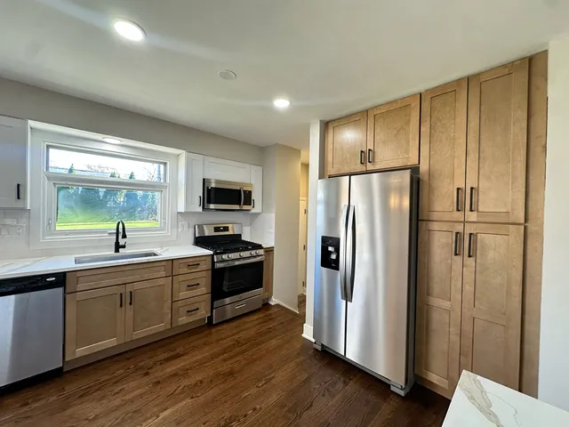 a kitchen with stainless steel appliances granite countertop a refrigerator a sink dishwasher a stove and a refrigerator with wooden floor