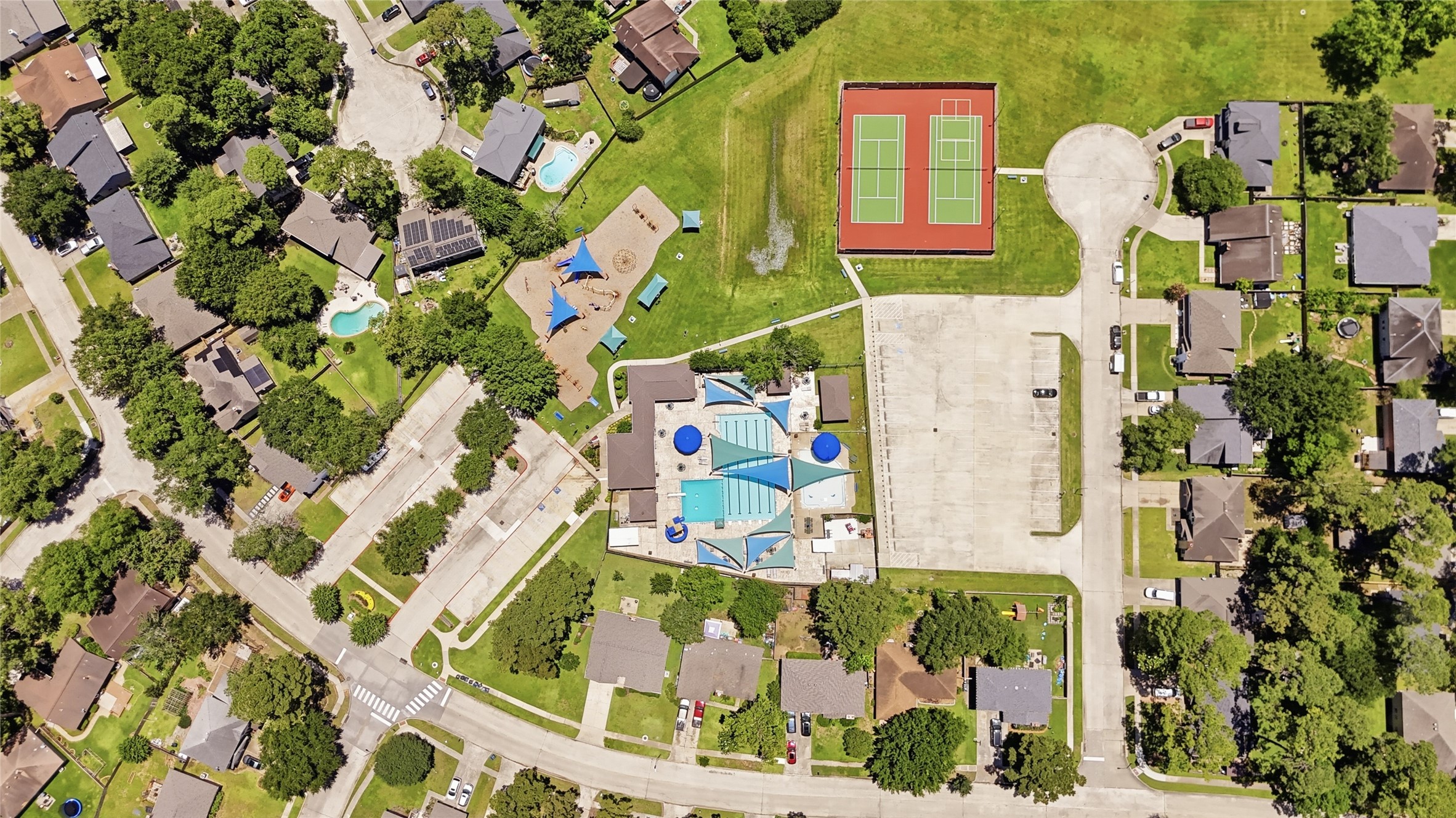 4718 Temple Bell Drive Spring, TX 77388 - Photo 49 of 50 This aerial view showcases a suburban neighborhood with tree-lined streets, well-maintained homes, and community amenities. There's a central recreational area featuring a swimming pool, tennis courts, and a playground, surrounded by lush greenery.