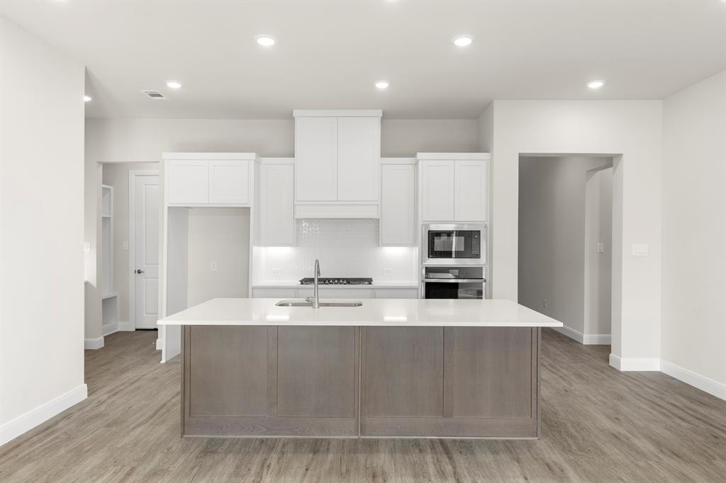 1201 Century Tree Lane Anna, TX 75409 - Photo 7 of 26 a large kitchen with kitchen island a stove a refrigerator a sink and white cabinets with wooden floor