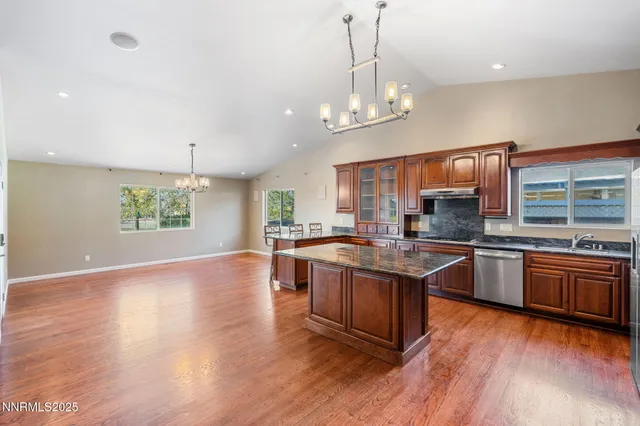a large kitchen with stainless steel appliances granite countertop a stove a sink dishwasher a refrigerator and a dining table with wooden floor