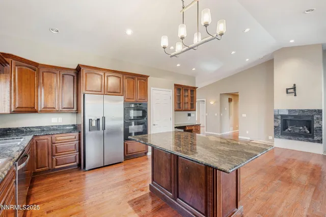 a kitchen with kitchen island granite countertop a refrigerator a stove a sink a dining table and chairs with wooden floor