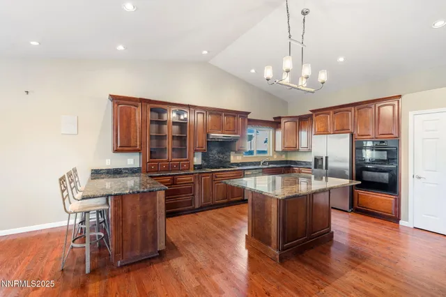 a kitchen with stainless steel appliances granite countertop a refrigerator a stove top oven a sink dishwasher a dining table and chairs with wooden floor
