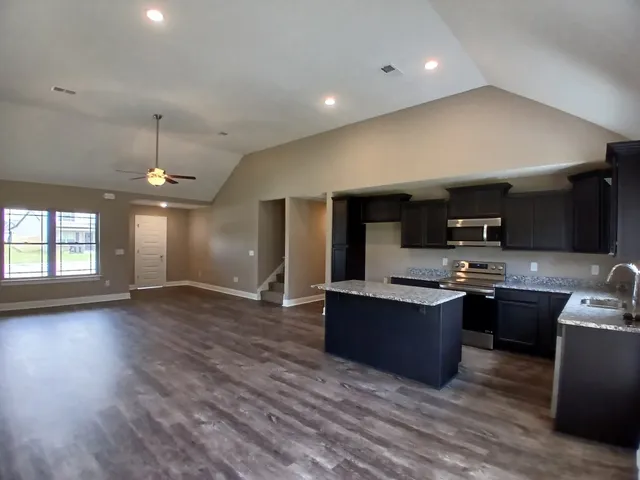 a kitchen with stainless steel appliances granite countertop wooden cabinets a sink a stove a microwave and wooden floors