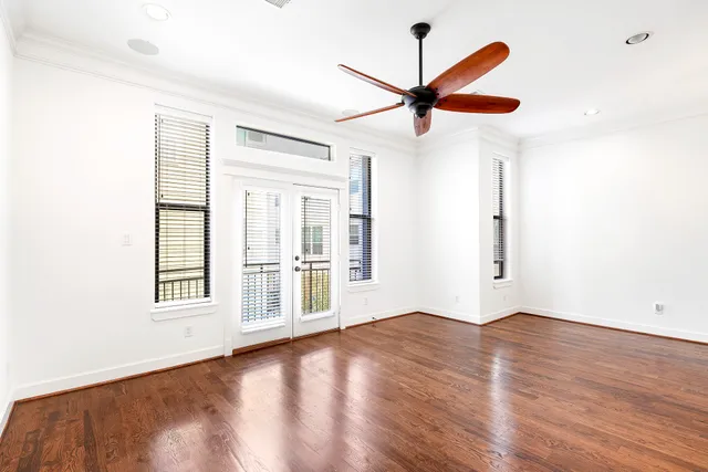 an empty room with wooden floor fan and windows