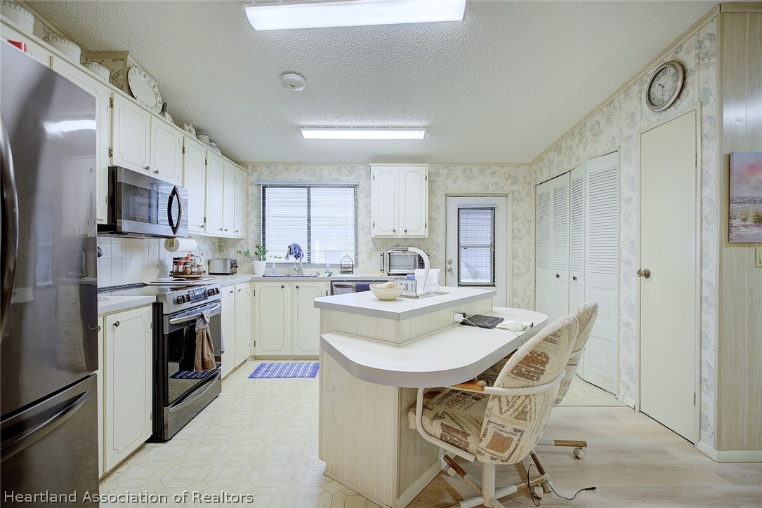 1571 Caribbean Road Sebring, FL 33870 - Photo 14 of 41 a kitchen with stainless steel appliances a sink a stove a refrigerator cabinets and chairs