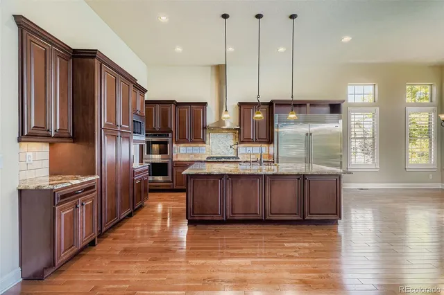 a kitchen with stainless steel appliances granite countertop a refrigerator a sink dishwasher a oven and a kitchen island with wooden floor