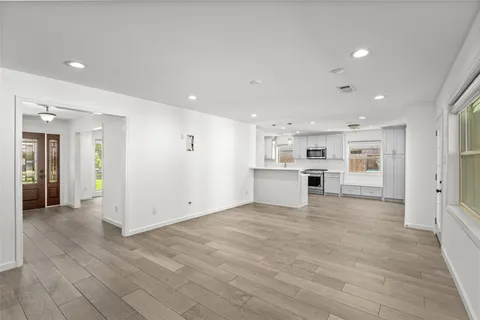 a view of an empty room with wooden floor and a kitchen