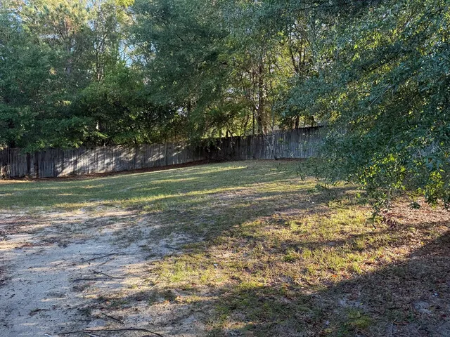 a view of a backyard with large trees and wooden fence