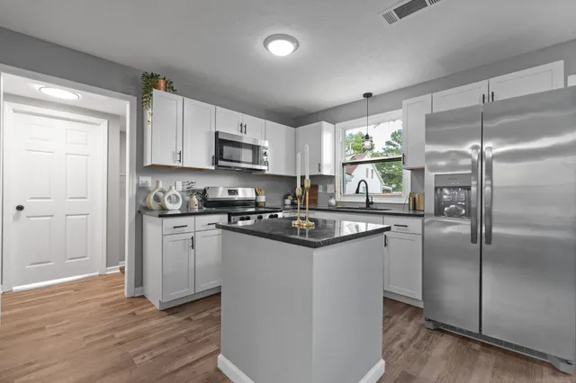 a kitchen with kitchen island granite countertop a refrigerator a sink a stove a microwave and cabinets