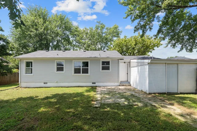 a view of a yard in front of a house with plants and large tree