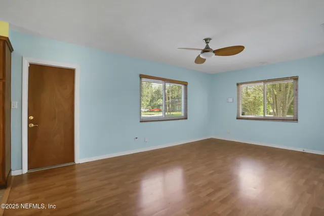 an empty room with wooden floor ceiling fan and windows