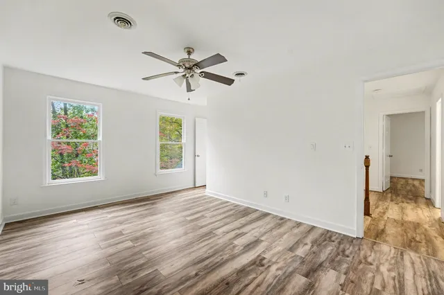 an empty room with wooden floor ceiling fan and windows